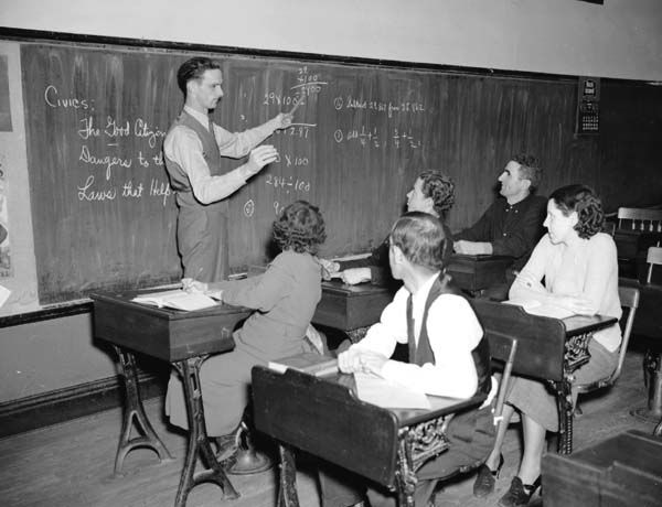 A teacher standing at a chalkboard in front of a classroom.