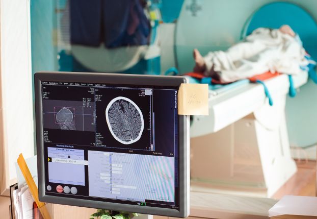 Stock photo an MRI machine with patient and screen in the foreground.